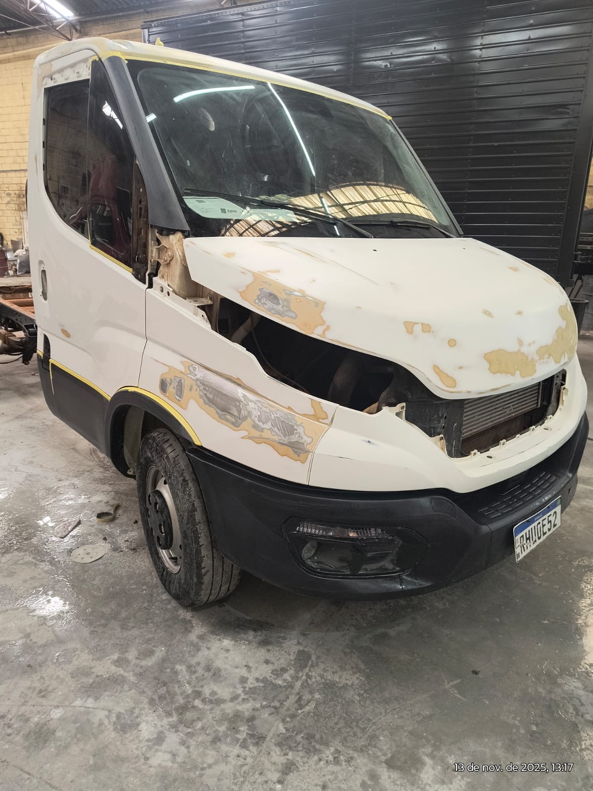 caminhão Iveco branco em restauração de funilaria numa oficina, com massa aplicada no capô e lataria parcialmente desmontada