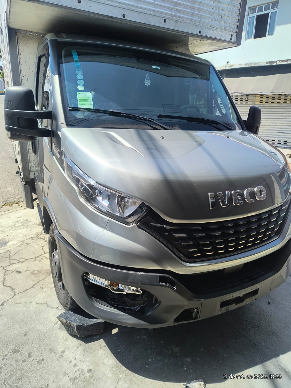 caminhão bau prata IVECO estacionado na rua em frente a lojas com persianas fechadas